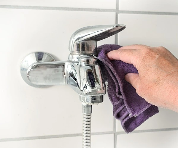 Photo de quelqu'un qui nettoie le calcaire sur un robinet de salle de bain