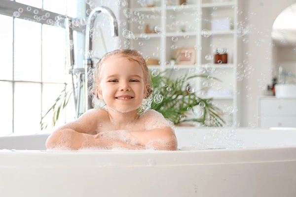 photo d'un enfant souriant dans son bain , accoudé à la baignoire, avec des bulles de savon autour de lui