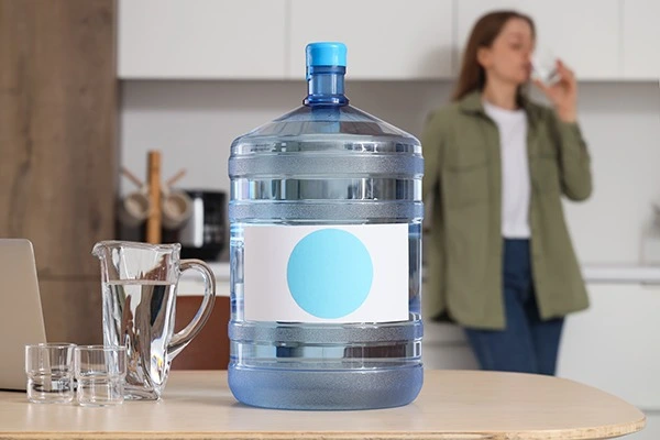 Photo d'une bouteille d'eau en plastique, femme qui boit un verre d'eau en arrière plan